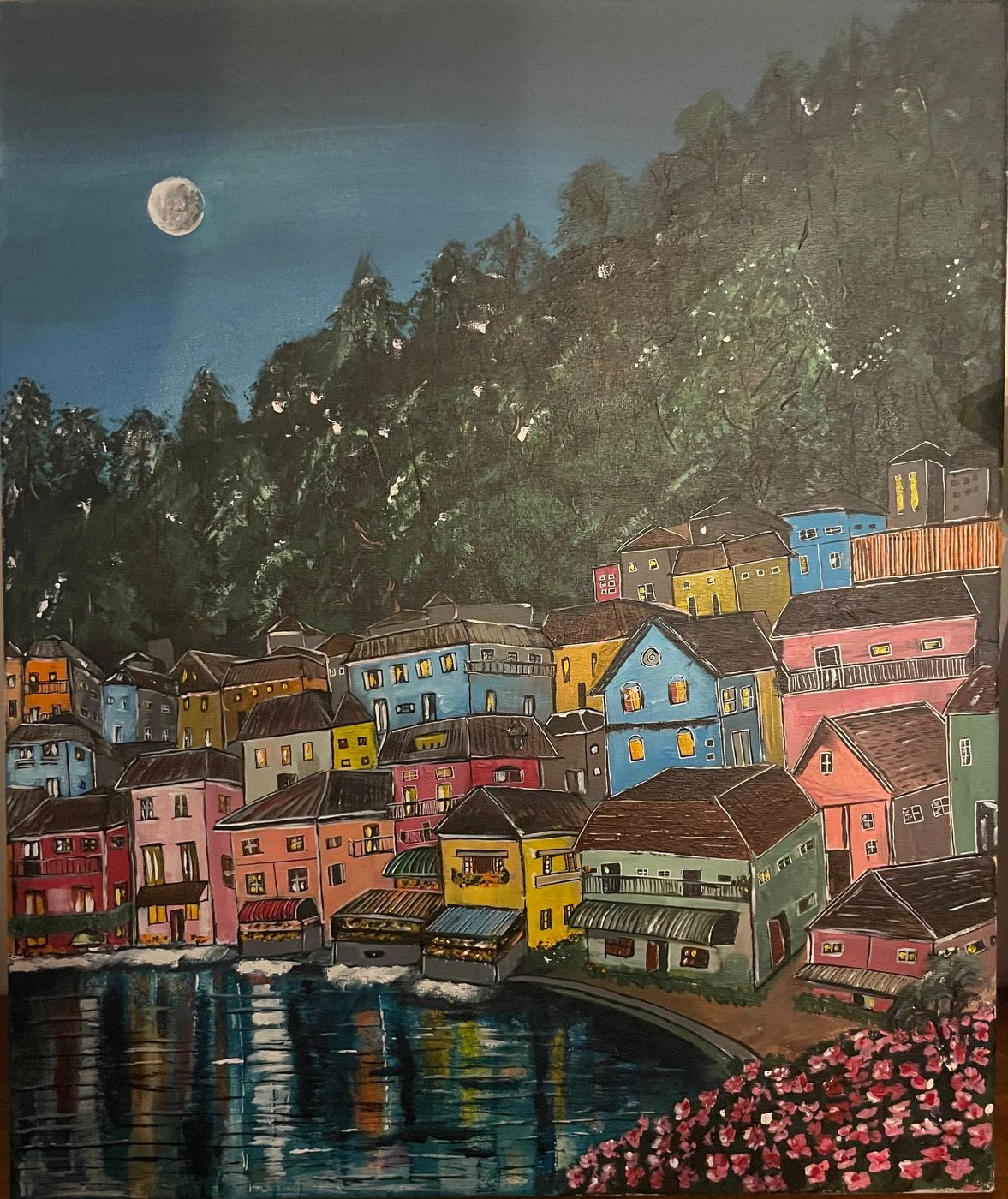 Harbour Lanterns by Deepti Dasika: Moonlit harbour town: stacked pastel houses glowing at the waterline, dark forested hill, pink blossoms in the foreground.